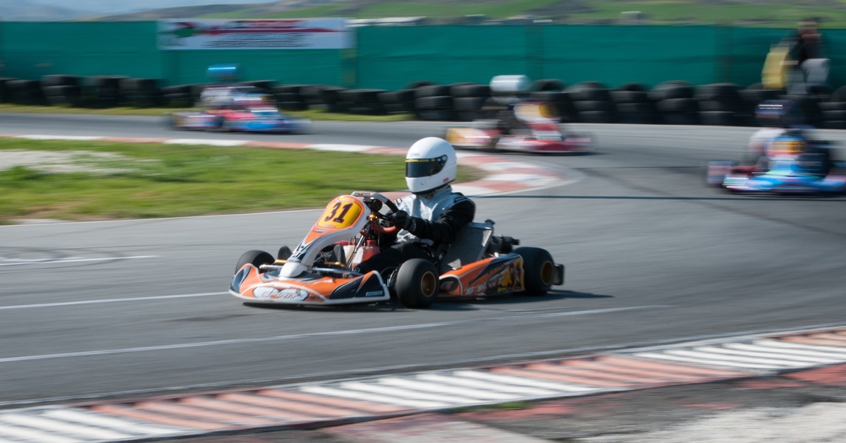 A racer in a black suit speeding through a corner in kart number 31 on an outdoor track with tire walls and banners.