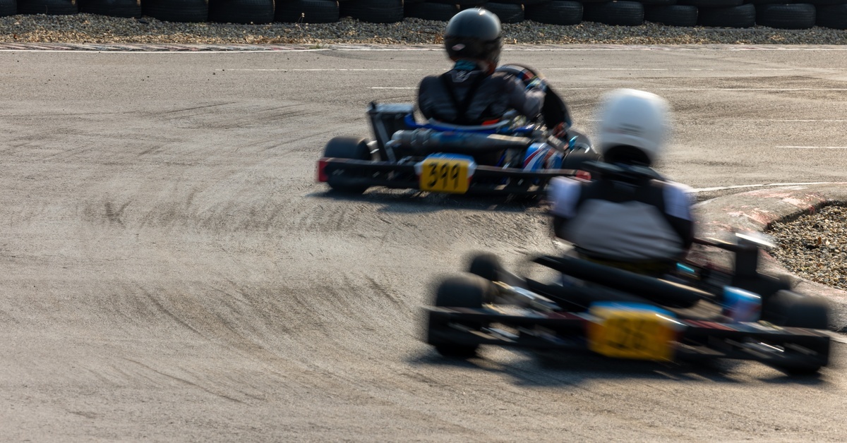 Two people racing go karts on a track. Both drivers are approaching a curve and turning right.